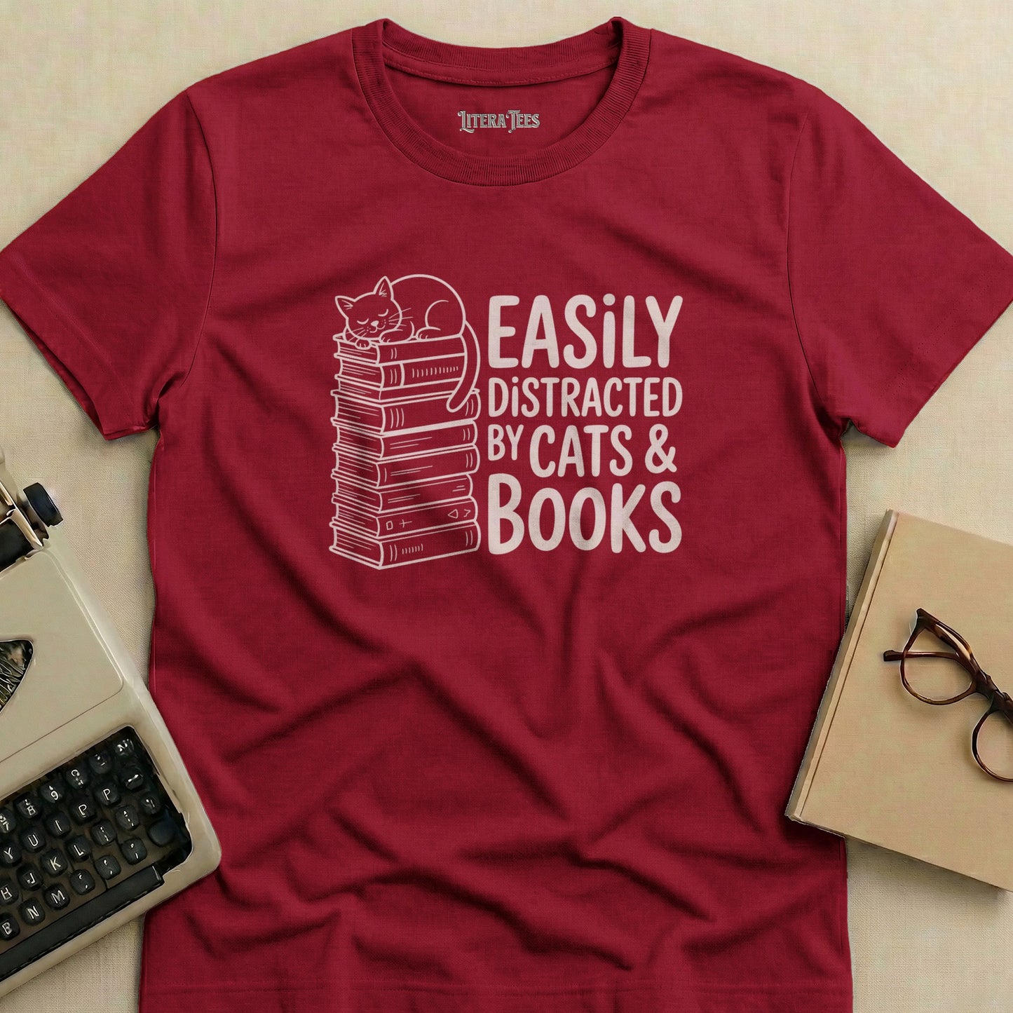 Maroon t-shirt with white text "Easily Distracted By Cats & Books" and a cat sleeping on a stack of books.