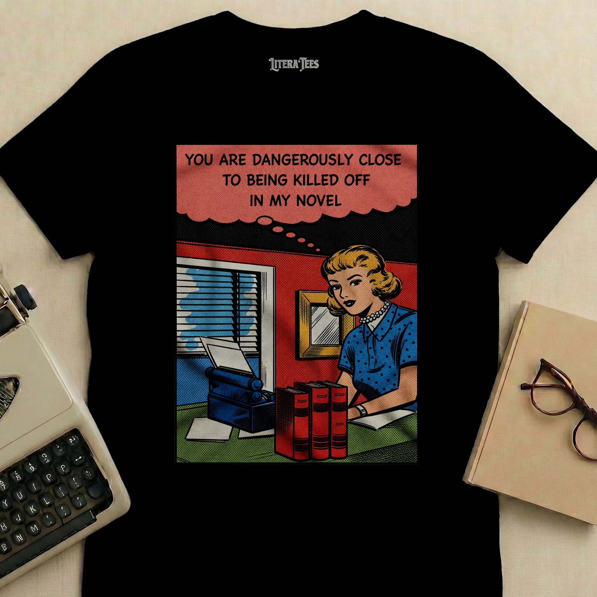 T-shirt with cartoon of woman at typewriter, text "YOU ARE DANGEROUSLY CLOSE TO BEING KILLED OFF IN MY NOVEL".