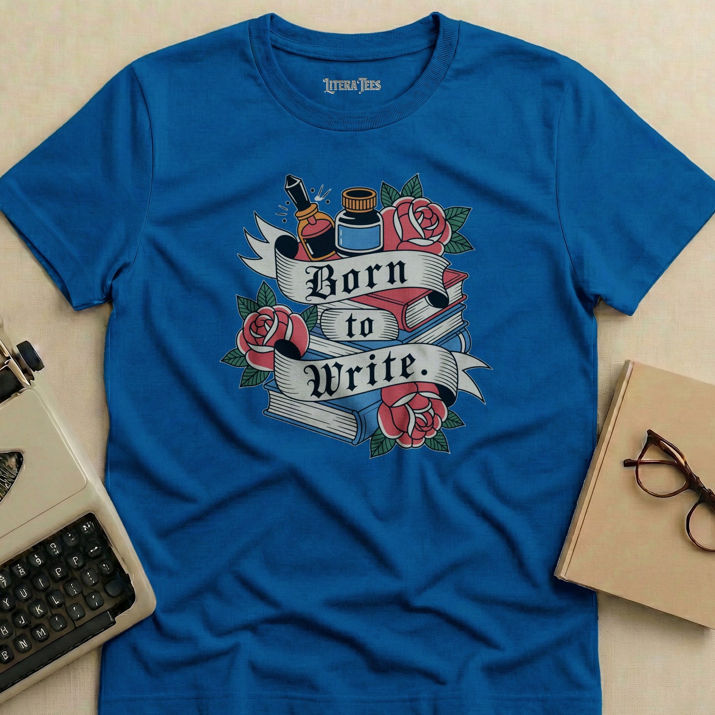 Blue t-shirt with "Born to Write" text, books, roses, and ink bottle graphic.