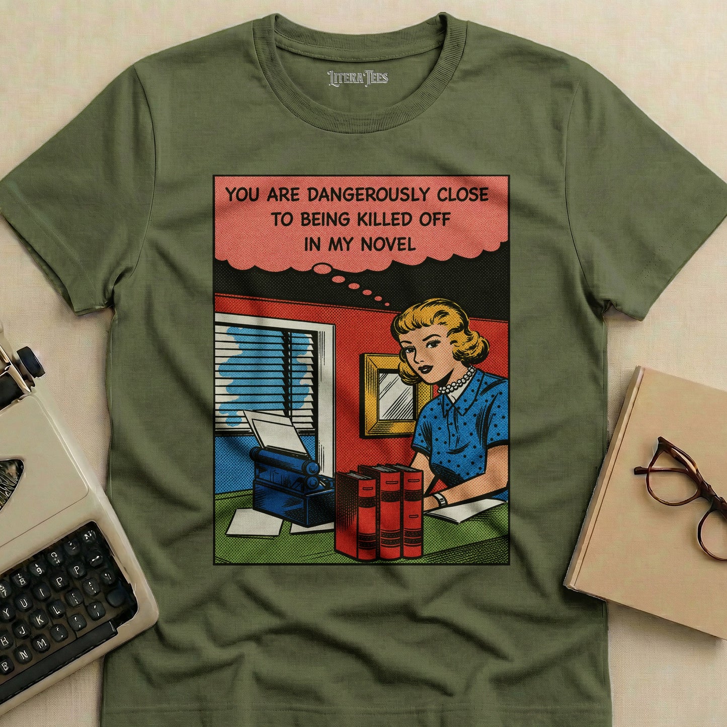 T-shirt with comic book panel: woman at desk, text reads "You are dangerously close to being killed off in my novel."