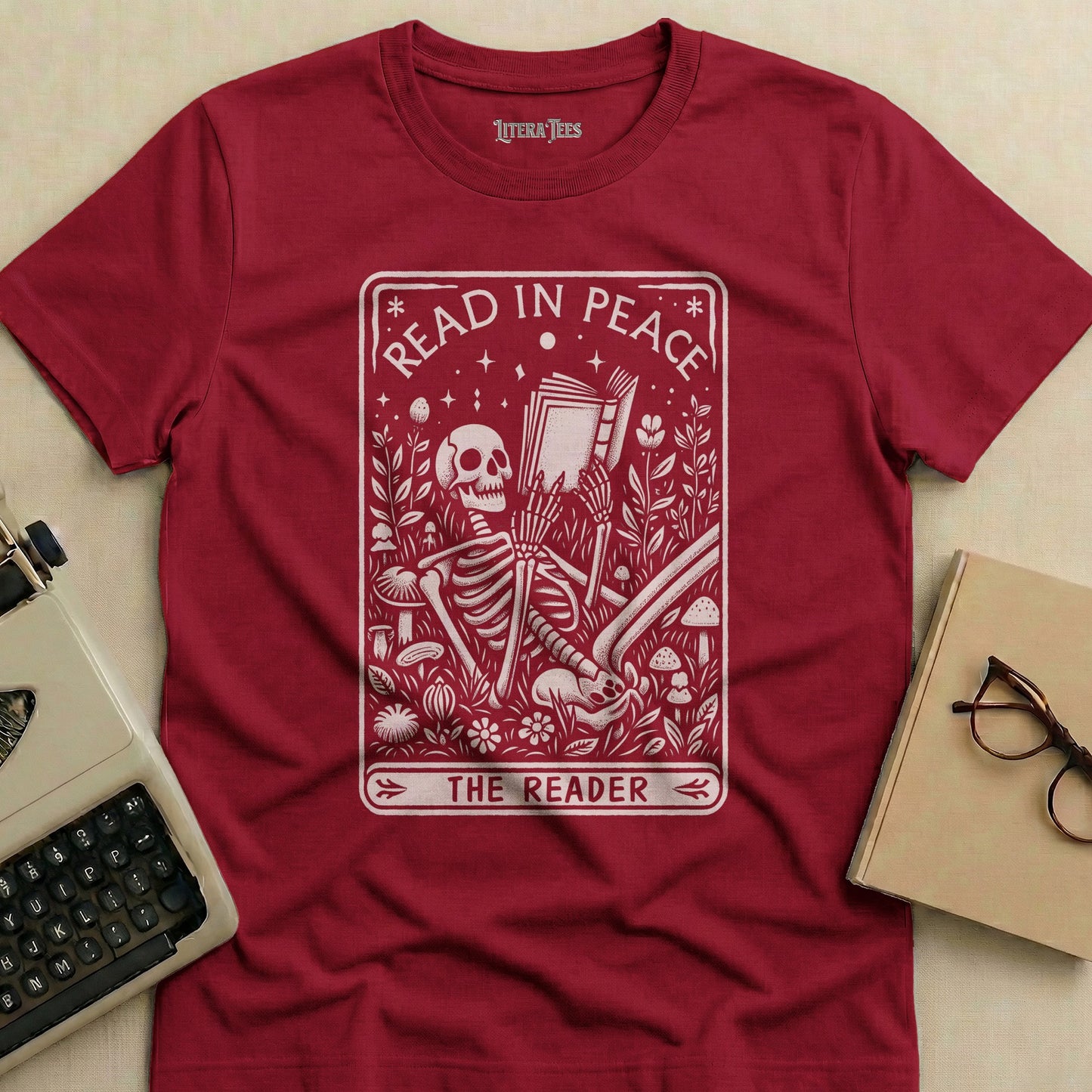 Maroon t-shirt with "Read in Peace The Reader" text and skeleton reading surrounded by plants.