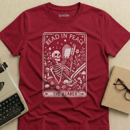 Maroon t-shirt with "Read in Peace The Reader" text and skeleton reading surrounded by plants.