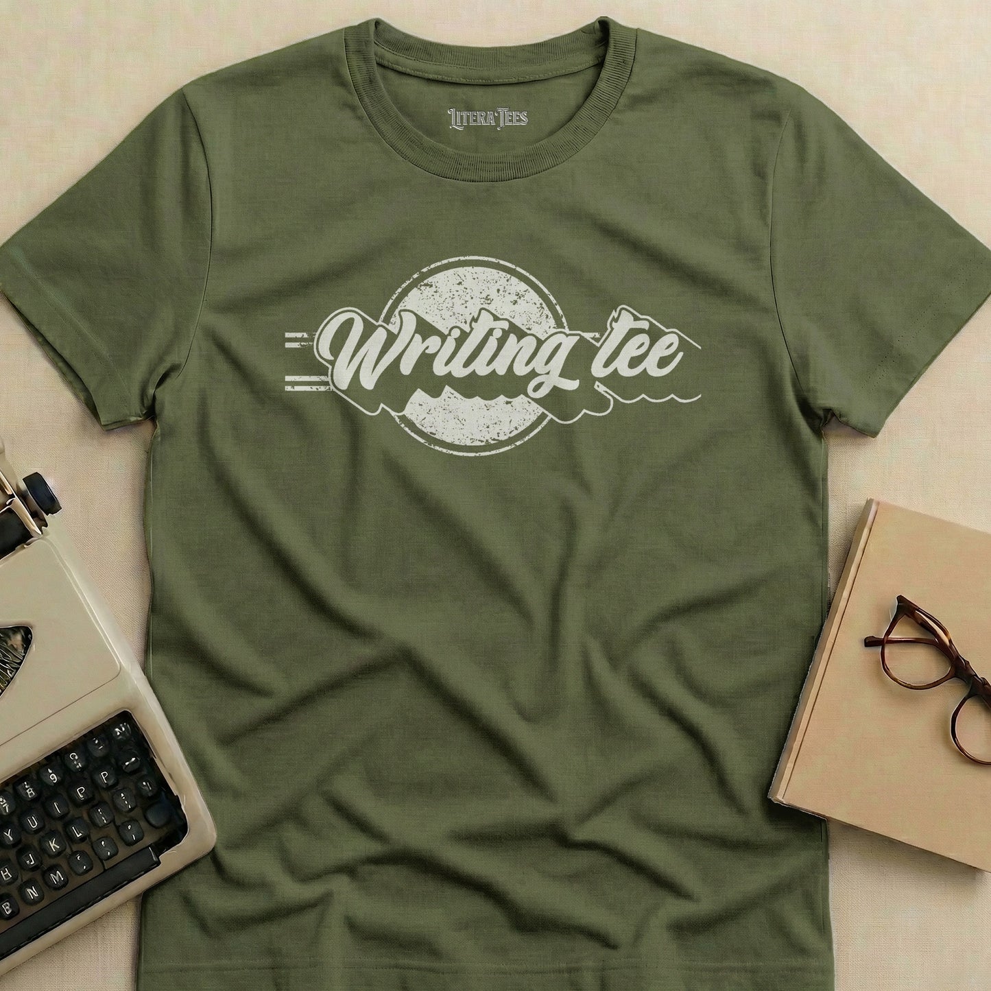 Olive green t-shirt with "Writing Tee" graphic and typewriter and glasses nearby.
