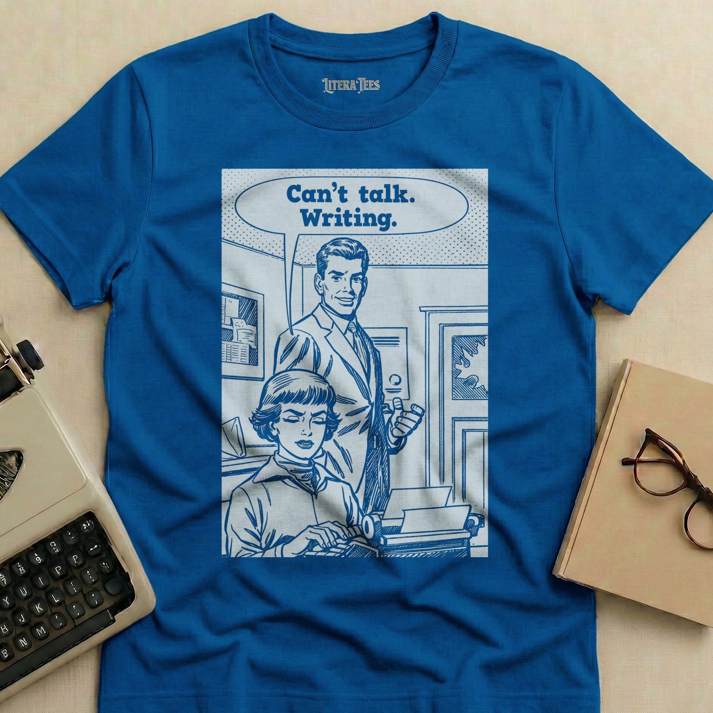 Blue t-shirt with graphic of people at a typewriter, text "Can't talk. Writing."