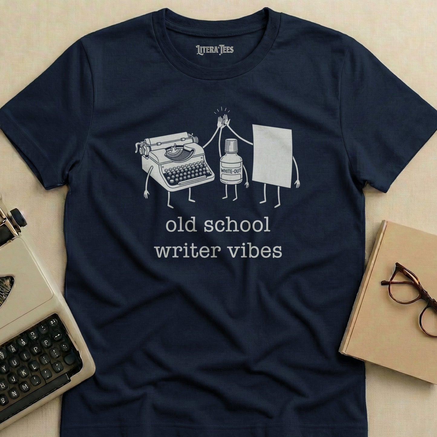 Navy t-shirt with cartoon typewriter and White-Out pen giving a high-five, saying "old school writer vibes".