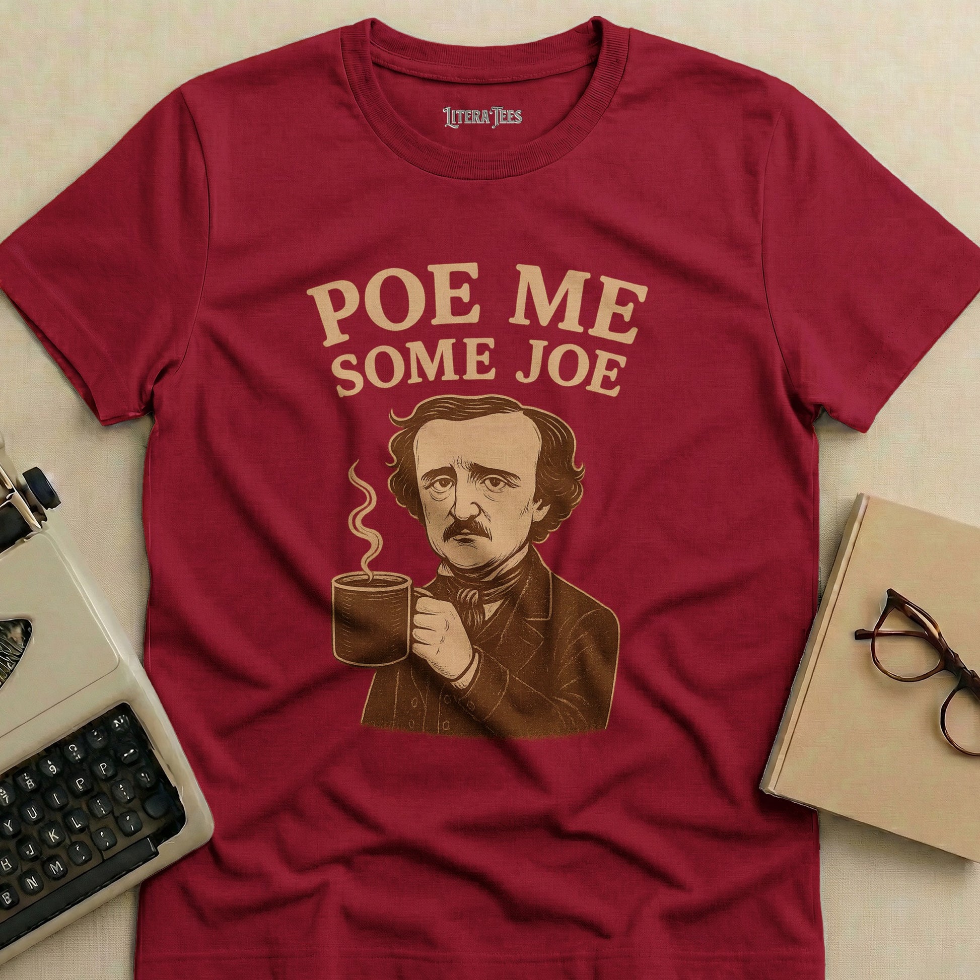 Edgar Allan Poe holding a coffee cup on a burgundy t-shirt with "Poe Me Some Joe" text.