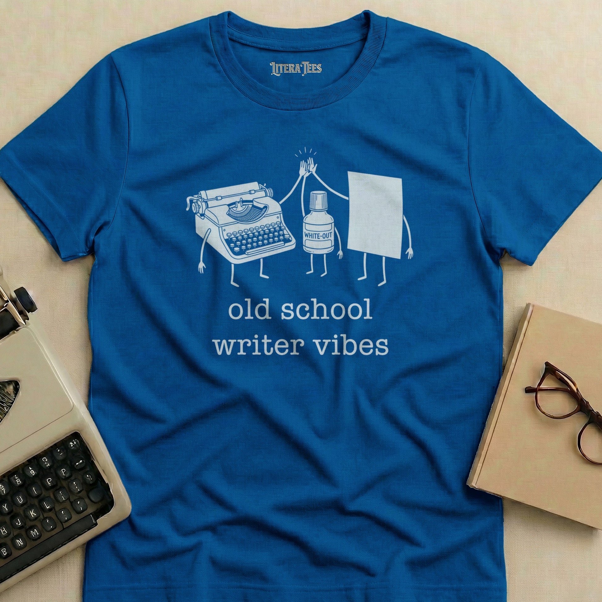 Blue t-shirt with "old school writer vibes" and illustrations of typewriter and White-Out.