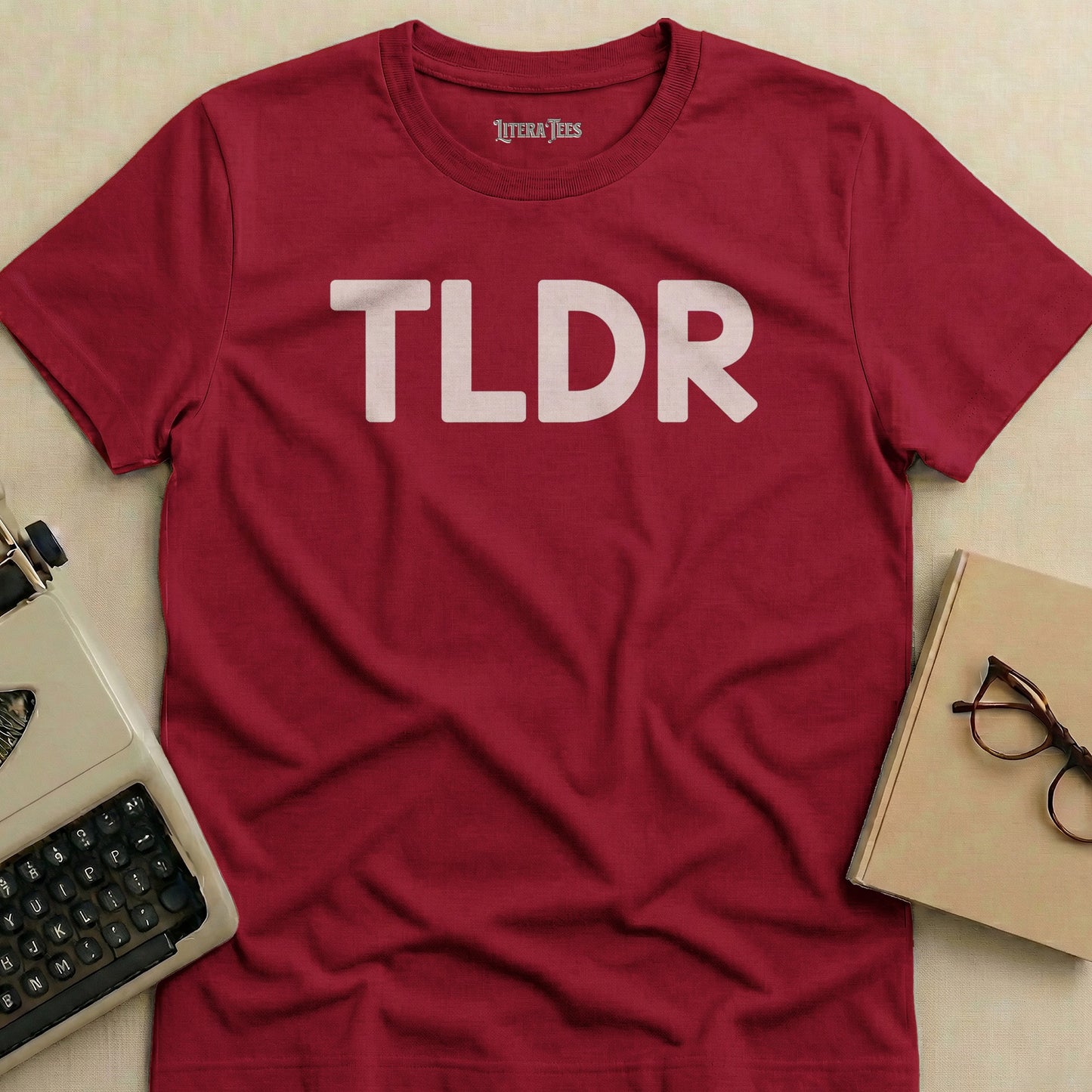 Red t-shirt with white "TLDR" text and glasses on a table.