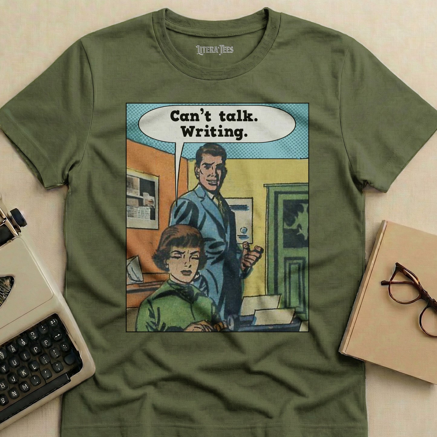 Olive green t-shirt with comic illustration of a man and woman, "Can't talk. Writing."