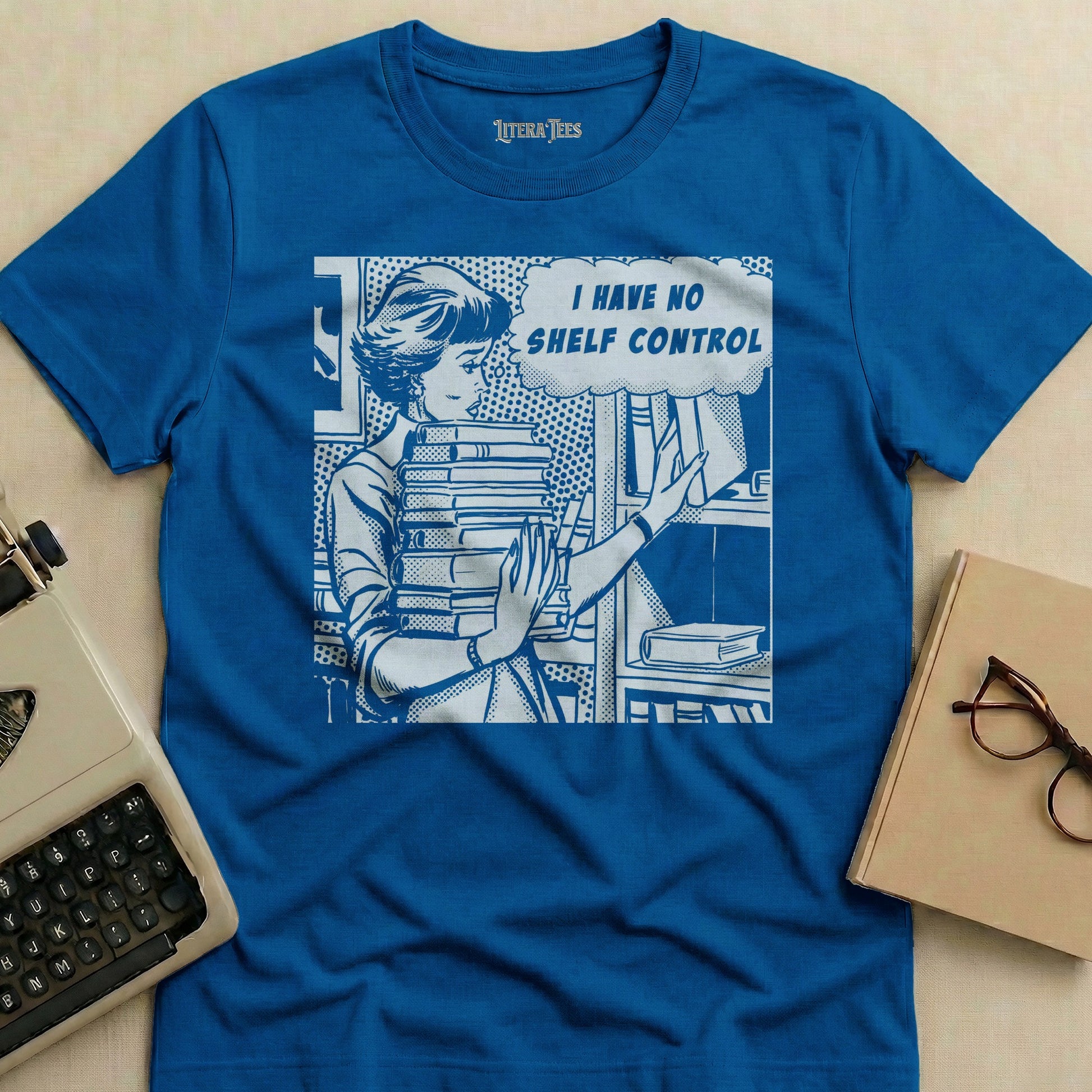 Blue t-shirt with comic book style woman holding books, text "I HAVE NO SHELF CONTROL".