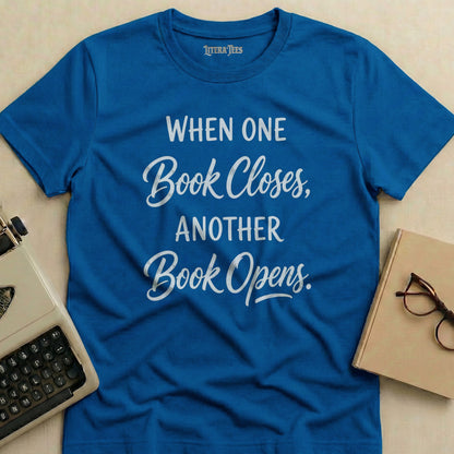 Blue t-shirt with white text "When One Book Closes, Another Book Opens."