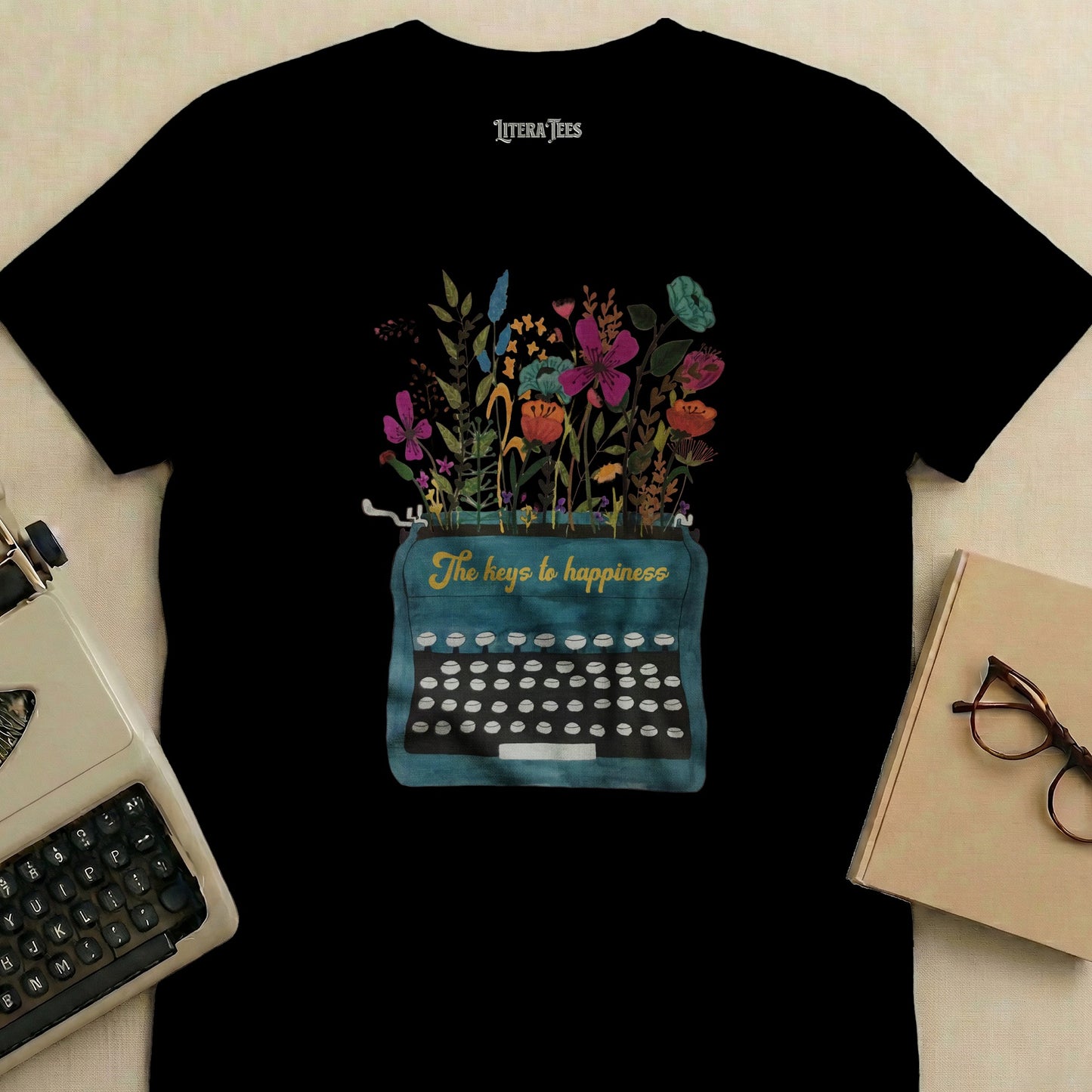 Black t-shirt with a teal typewriter graphic featuring flowers and "The keys to happiness" text.