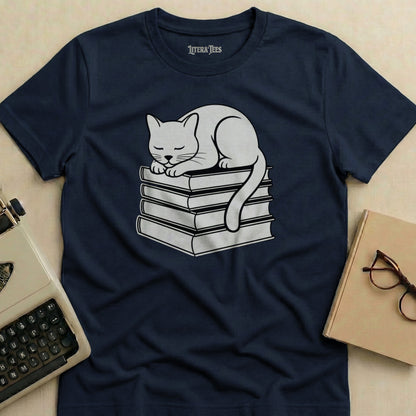 Cat sleeping on a stack of books, dark blue t-shirt.