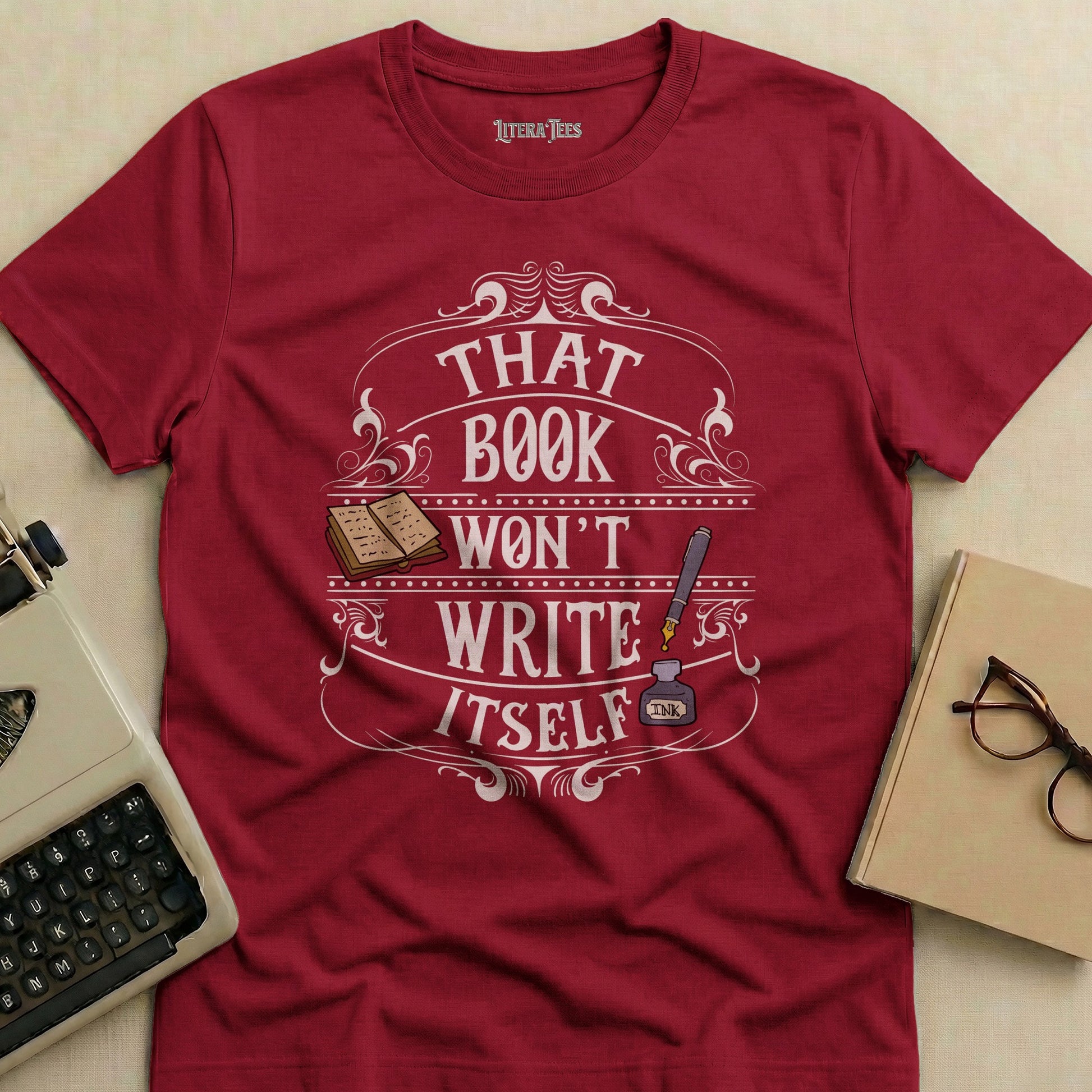 Burgundy t-shirt with text "That book won't write itself" and illustration.