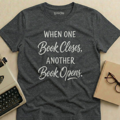T-shirt with white text "When One Book Closes, Another Book Opens."