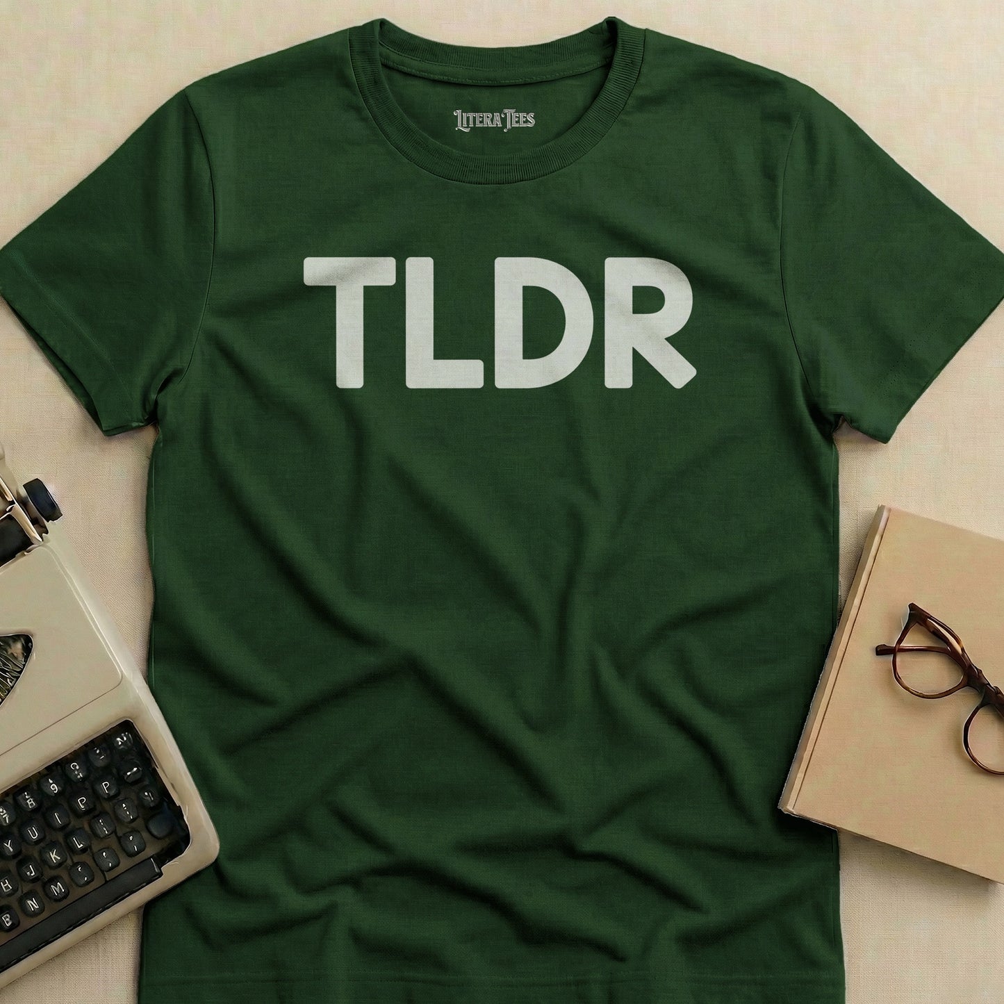 Dark green t-shirt with "TLDR" printed in white, next to a typewriter and glasses.