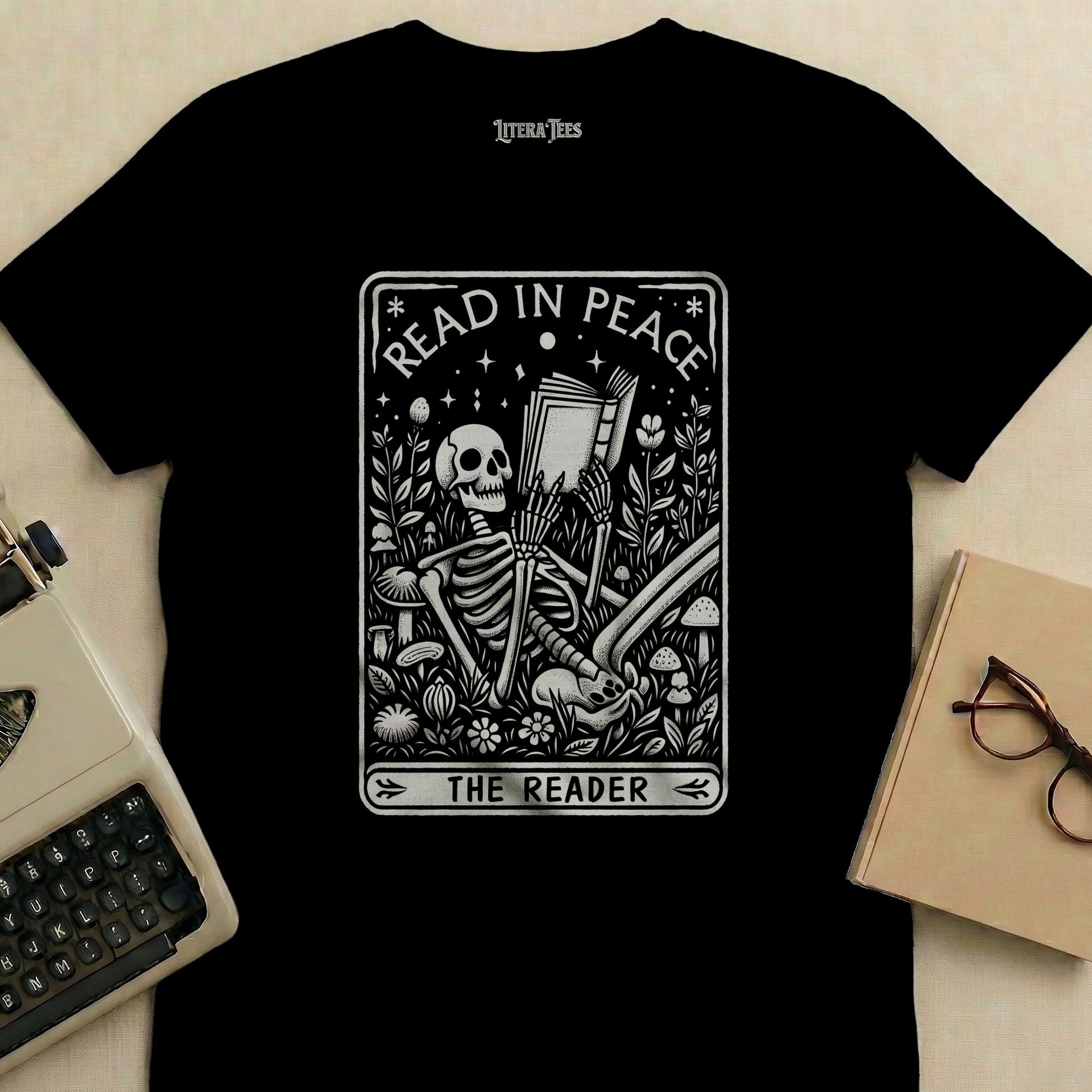 Black t-shirt graphic of a skeleton reading a book, surrounded by plants and mushrooms.