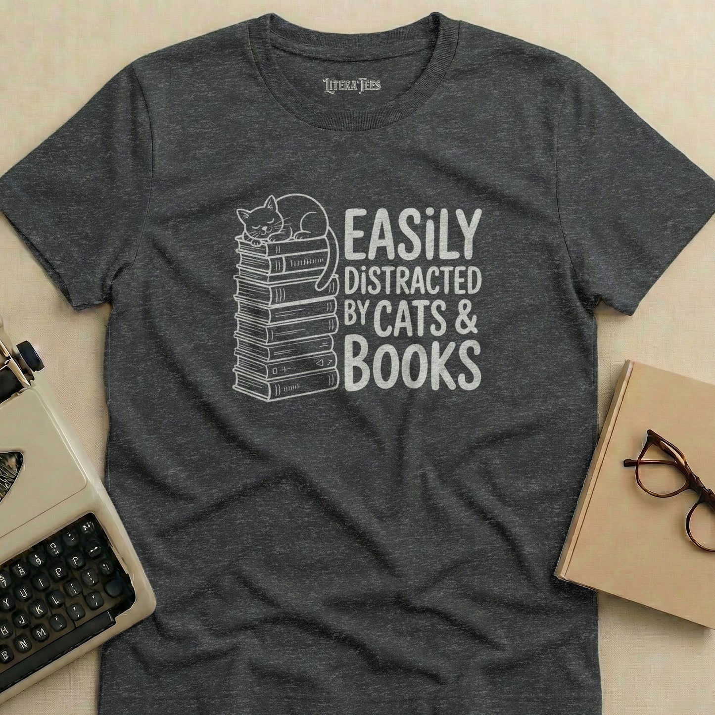 Dark grey t-shirt with white text and illustration of cat on stack of books.