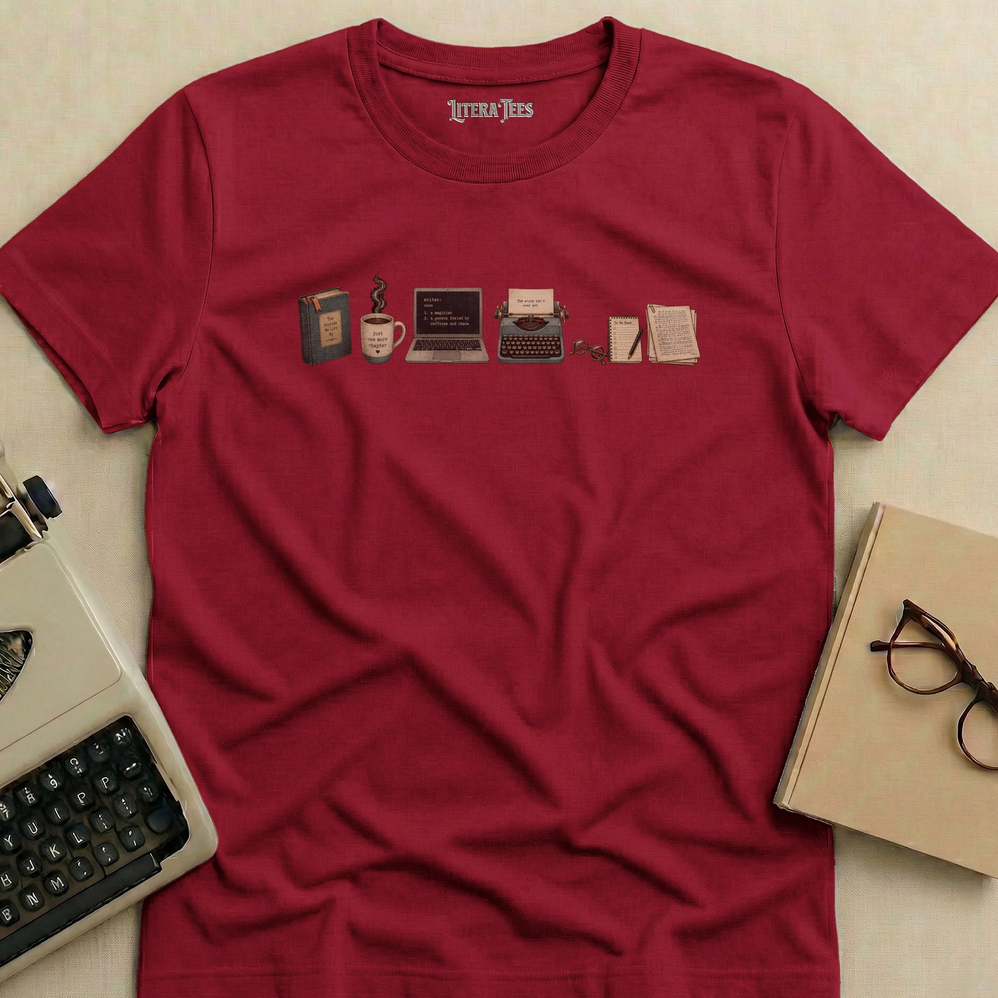 Maroon t-shirt with literary icons: book, coffee, laptop, typewriter, and notebooks.