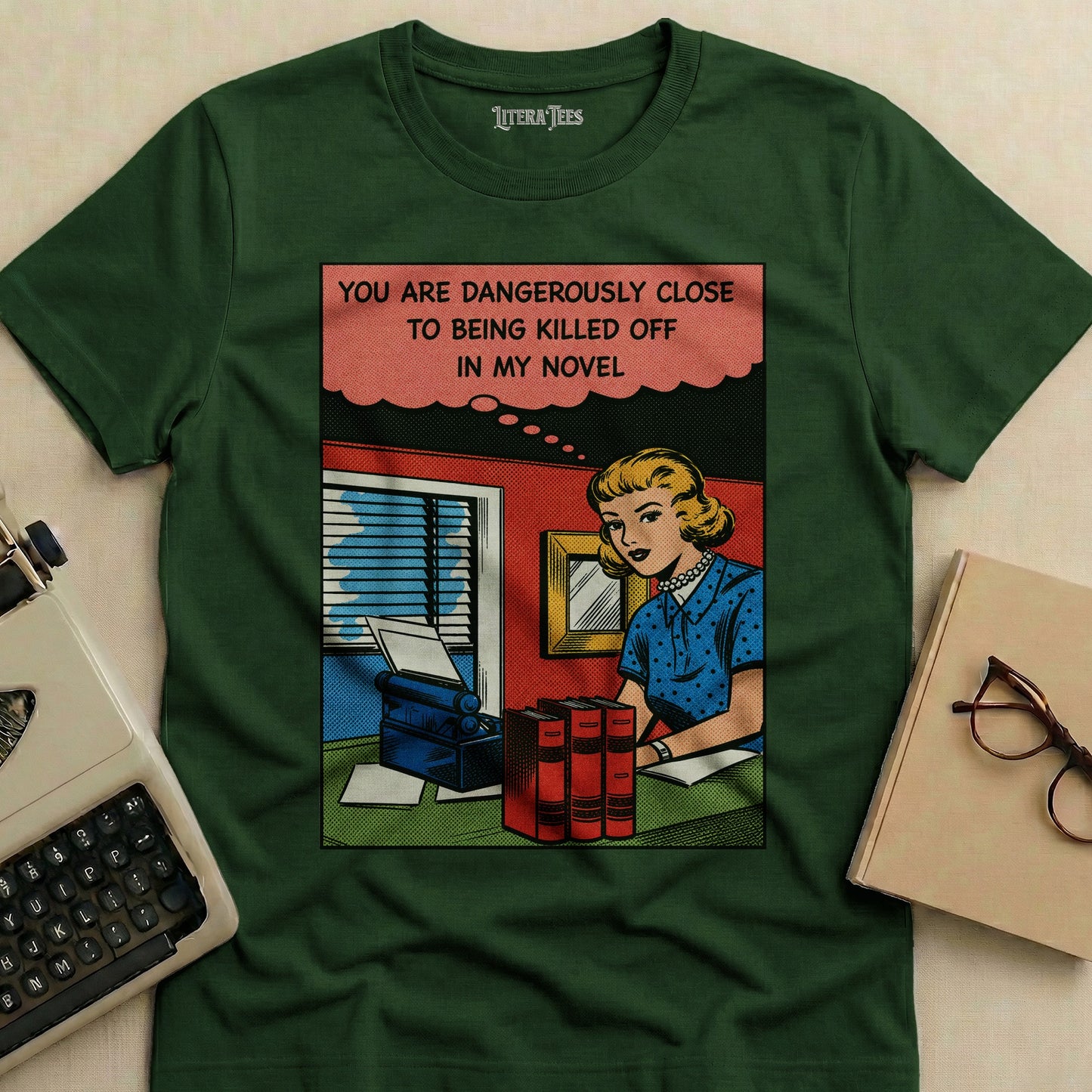 Green t-shirt with comic book style graphic: woman at typewriter, text about being killed off in a novel.