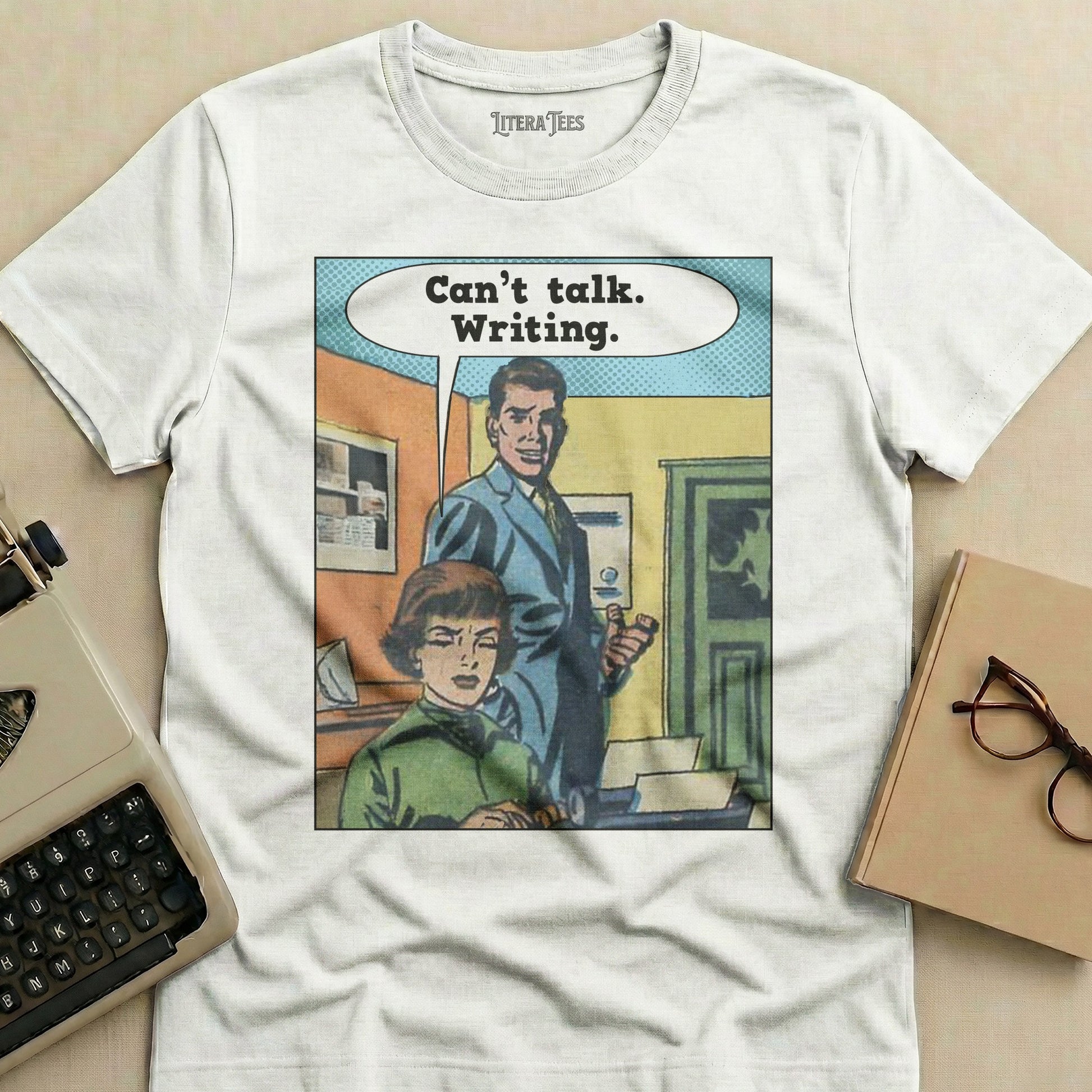 T-shirt with comic panel: woman seated, man standing, text reads "Can't talk. Writing."