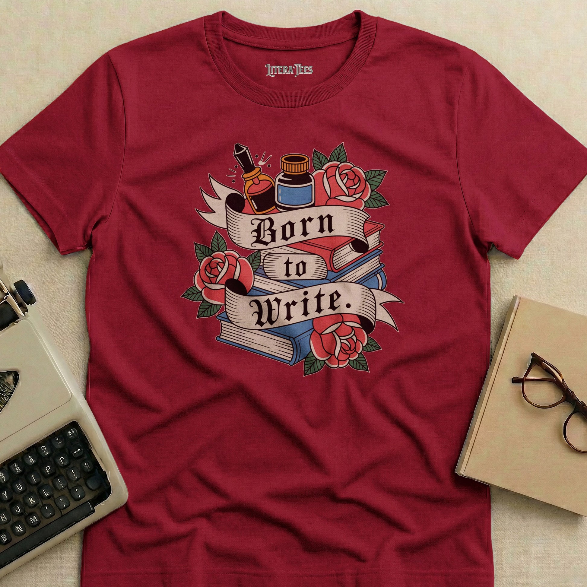 Maroon t-shirt with "Born to Write." text, books, roses, and inkwell design.