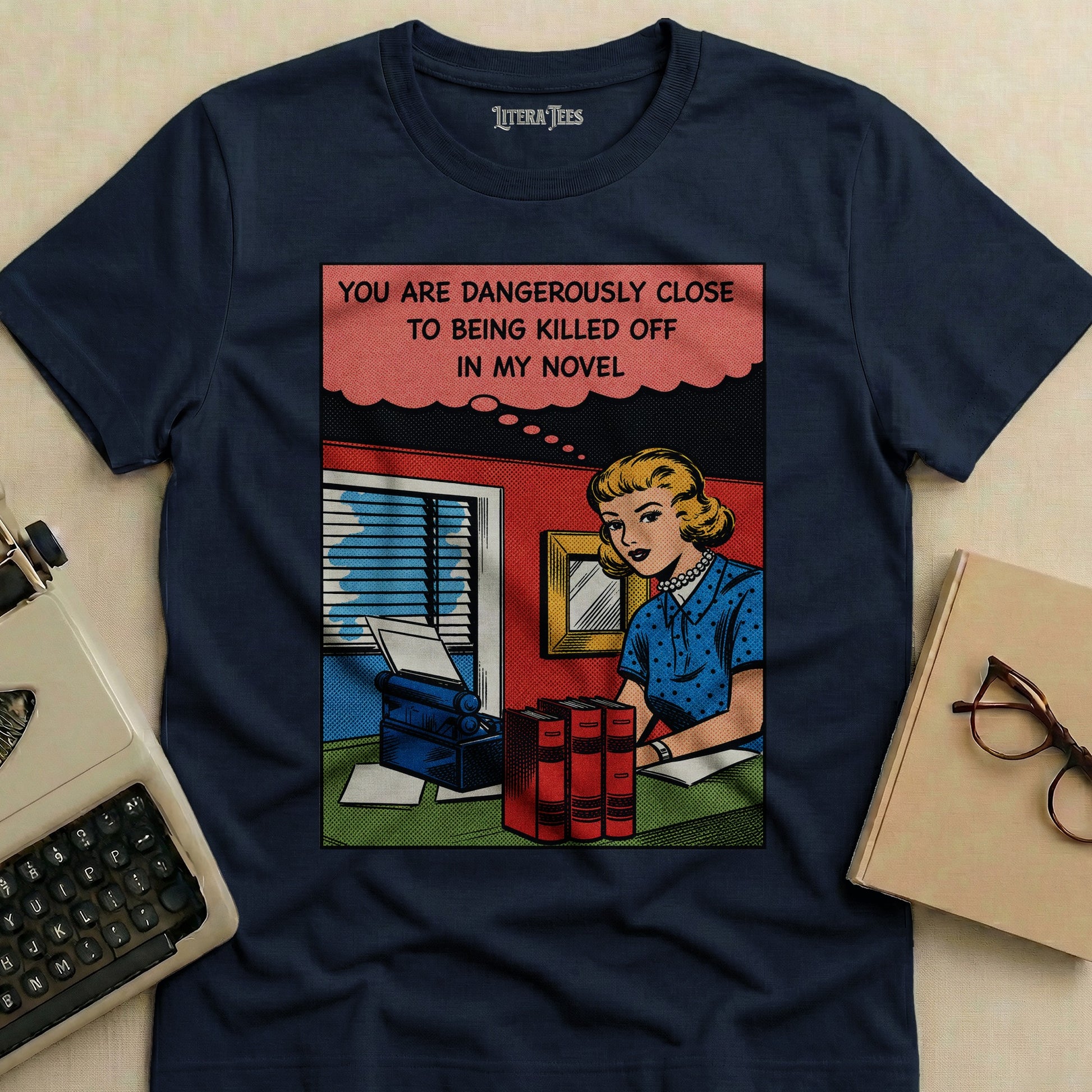 T-shirt with comic panel illustration of a woman at a typewriter, text "YOU ARE DANGEROUSLY CLOSE TO BEING KILLED OFF IN MY NOVEL".
