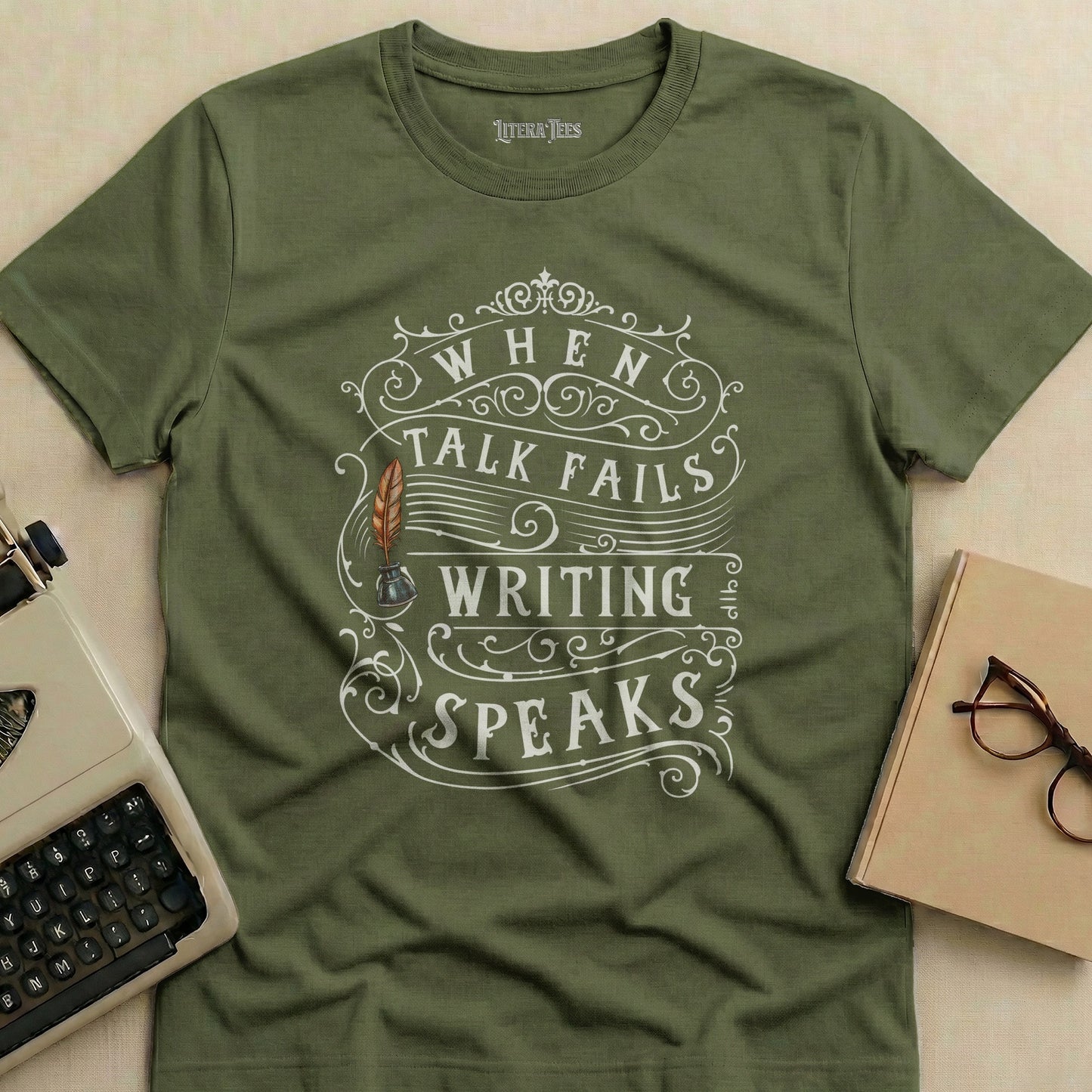 Olive green t-shirt with "When talk fails, writing speaks" text and quill design.